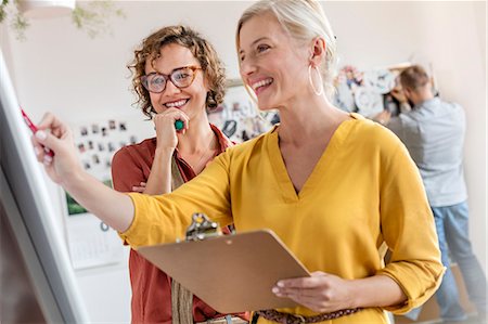 Smiling female design professionals with clipboard meeting at flipchart in office Stock Photo - Premium Royalty-Free, Code: 6113-08805856