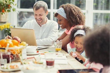 simsearch:6113-07730780,k - Smiling young multi-ethnic family using laptop and eating breakfast at table Stock Photo - Premium Royalty-Free, Code: 6113-08943686