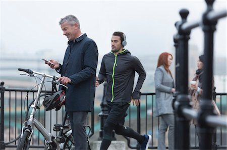 Businessman with bicycle texting with cell phone and male runner on urban ramp Stock Photo - Premium Royalty-Free, Code: 6113-08943761