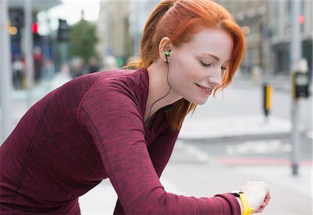 runners resting - Smiling female runner with red hair and headphones checking smart watch Stock Photo - Premium Royalty-Free, Code: 6113-08943777