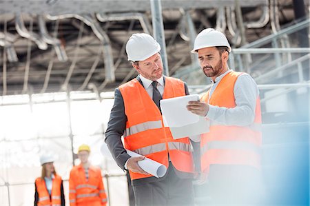 reflective clothing - Male engineers with blueprints and clipboard discussing paperwork at construction site Stock Photo - Premium Royalty-Free, Code: 6113-08943923