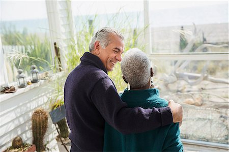 seniors back interior - Senior couple hugging on sunny beach house sun porch Stock Photo - Premium Royalty-Free, Code: 6113-08985730