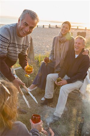 Smiling mature couples drinking wine and barbecuing on sunset beach Stock Photo - Premium Royalty-Free, Code: 6113-08985819