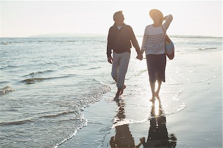 simsearch:6113-07589470,k - Affectionate mature couple holding hands and walking on sunset ocean beach surf Stock Photo - Premium Royalty-Free, Code: 6113-08985830