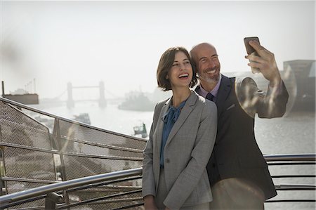 simsearch:632-07674444,k - Enthusiastic, smiling business couple taking selfie with camera phone on sunny urban bridge, London, UK Stock Photo - Premium Royalty-Free, Code: 6113-08985983
