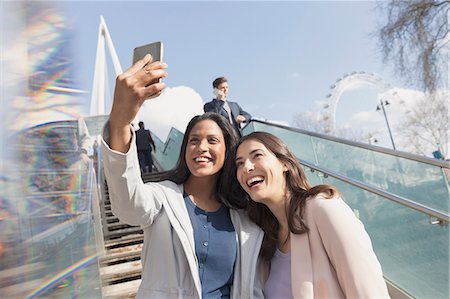Enthusiastic, smiling women friends taking selfie with camera phone on sunny, urban stairs, London, UK Stock Photo - Premium Royalty-Free, Code: 6113-08985986
