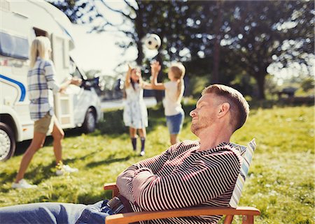 Serene father resting in lounge chair with family playing in background outside sunny motor home Foto de stock - Sin royalties Premium, Código: 6113-08909930