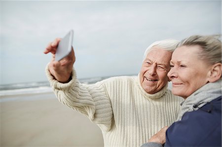 senior couple posing - Senior couple taking selfie with cell phone on windy winter beach Stock Photo - Premium Royalty-Free, Code: 6113-08910060