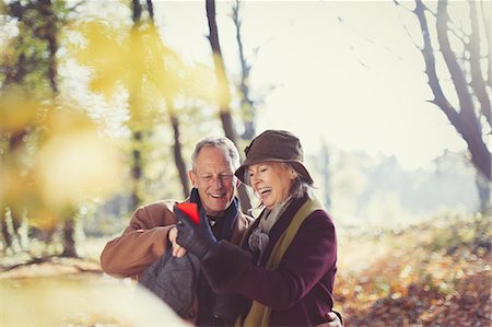 simsearch:6113-08743448,k - Smiling senior couple using cell phone in sunny autumn park Stock Photo - Premium Royalty-Free, Code: 6113-08910097