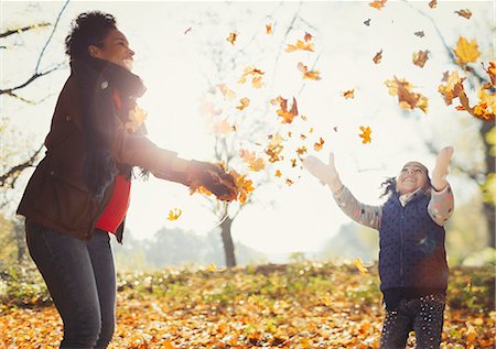 Playful mother and daughter throwing autumn leaves in sunny park Stock Photo - Premium Royalty-Free, Code: 6113-08910103