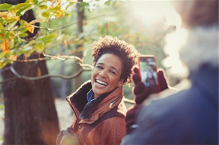 simsearch:6113-07565751,k - Smiling woman posing for boyfriend with camera phone in sunny autumn woods Stock Photo - Premium Royalty-Free, Code: 6113-08910121