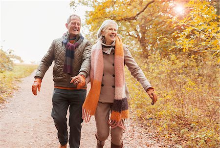 retired happy active - Smiling senior couple holding hands walking on path in autumn woods Stock Photo - Premium Royalty-Free, Code: 6113-08910139