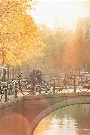 simsearch:6113-06498180,k - Young couple with bicycles taking selfie with selfie stick on bridge over canal in Amsterdam Stock Photo - Premium Royalty-Free, Code: 6113-08927643