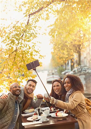 simsearch:632-07674444,k - Smiling friends taking selfie with selfie stick at autumn sidewalk cafe Stock Photo - Premium Royalty-Free, Code: 6113-08927720