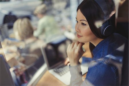 simsearch:6113-07565805,k - Pensive young woman at laptop listening to music with headphones at cafe window Stock Photo - Premium Royalty-Free, Code: 6113-09058435