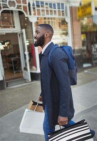 Smiling young man walking along storefront, carrying shopping bags Stock Photo - Premium Royalty-Free, Code: 6113-09058525