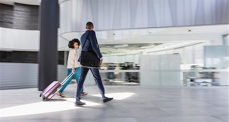 Businessman and businesswoman walking, pulling suitcase in modern office lobby Stock Photo - Premium Royalty-Free, Code: 6113-09058641