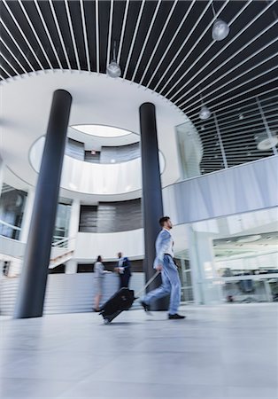 Businessman walking, pulling suitcase in architectural, modern office lobby Stock Photo - Premium Royalty-Free, Code: 6113-09058740