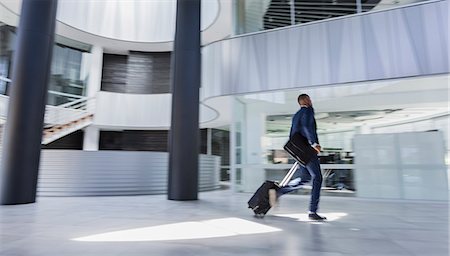 Businessman rushing, pulling suitcase in modern office lobby Stock Photo - Premium Royalty-Free, Code: 6113-09058732