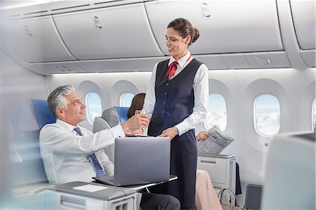 Flight attendant serving drink to businessman working at laptop on airplane Photographie de stock - Premium Libres de Droits, Code: 6113-09059152