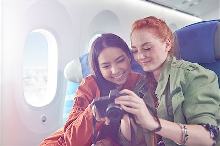 flying happy woman images - Smiling young women friends looking at photos on digital camera on airplane Stock Photo - Premium Royalty-Free, Code: 6113-09059173
