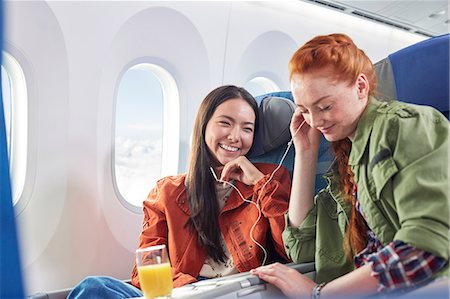 flying happy woman images - Young women friends sharing headphones, listening to music on airplane Stock Photo - Premium Royalty-Free, Code: 6113-09059190