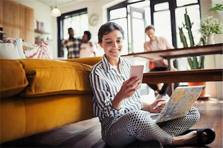 Smiling young woman using laptop and texting with smart phone on living room floor Stock Photo - Premium Royalty-Free, Code: 6113-09059428