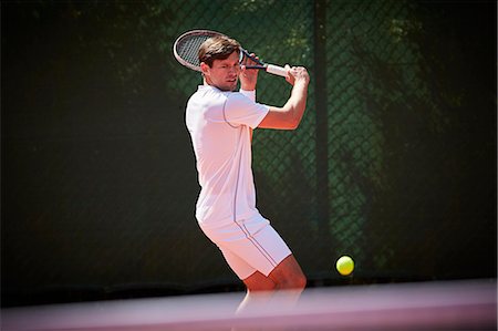 Young male tennis player playing tennis, swinging at tennis ball on sunny tennis court Stock Photo - Premium Royalty-Free, Code: 6113-09005118