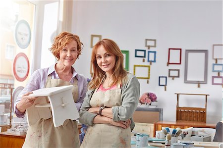 Portrait smiling, confident female artists holding painted bench in art class workshop Stock Photo - Premium Royalty-Free, Code: 6113-09005274