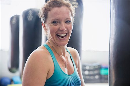 female boxing - Portrait laughing female boxer standing at punching bag in gym Stock Photo - Premium Royalty-Free, Code: 6113-09027379