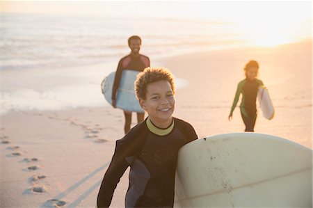 Portrait smiling pre-adolescent boy in wet suit carrying surfboard on summer sunset beach with family Foto de stock - Sin royalties Premium, Código: 6113-09027667