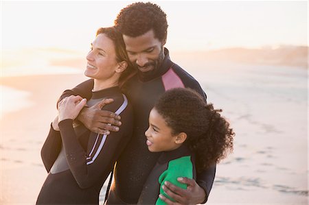simsearch:6113-06498556,k - Affectionate multi-ethnic family in wet suits hugging on sunset beach Stock Photo - Premium Royalty-Free, Code: 6113-09027671