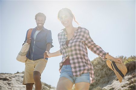 simsearch:6108-06166561,k - Smiling, affectionate multi-ethnic couple holding hands walking on sunny summer sand beach path Foto de stock - Sin royalties Premium, Código: 6113-09027682