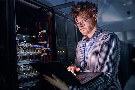 Focused male IT technician working at laptop in dark server room Stock Photo - Premium Royalty-Free, Code: 6113-09027615