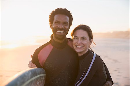 simsearch:6108-06166561,k - Portrait smiling, confident multi-ethnic couple with surfboard on sunny summer sunset beach Foto de stock - Sin royalties Premium, Código: 6113-09027746