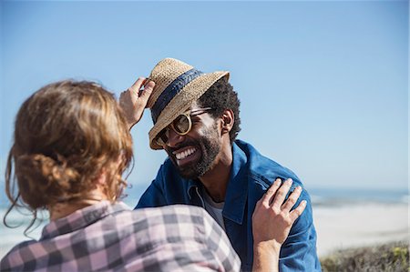 simsearch:632-05845211,k - Playful multi-ethnic couple with hat on sunny summer beach Stock Photo - Premium Royalty-Free, Code: 6113-09027711