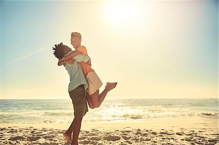 romantic lift hug - Playful boyfriend lifting girlfriend on sunny summer ocean beach Stock Photo - Premium Royalty-Free, Code: 6113-09027855