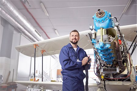 Portrait confident male airplane mechanic working on biplane in hangar Stock Photo - Premium Royalty-Free, Code: 6113-09027802