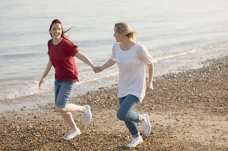 simsearch:6113-07589470,k - Playful lesbian couple holding hands and running on sunny beach Stock Photo - Premium Royalty-Free, Code: 6113-09199762