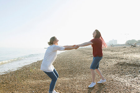 simsearch:6113-07589470,k - Playful lesbian couple holding hands and spinning on sunny beach Stock Photo - Premium Royalty-Free, Code: 6113-09199774