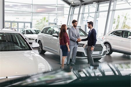 salesman customer car showroom - Car salesman and customers handshaking in car dealership showroom Stock Photo - Premium Royalty-Free, Code: 6113-09111753
