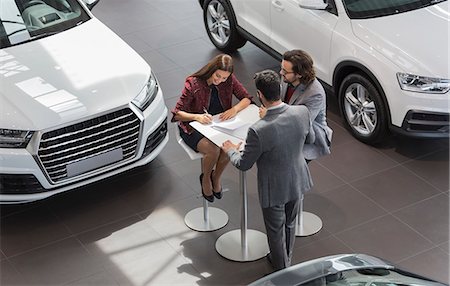simsearch:649-07119150,k - Car salesman watching couple customers signing financial contract paperwork in car dealership showroom Stock Photo - Premium Royalty-Free, Code: 6113-09111850