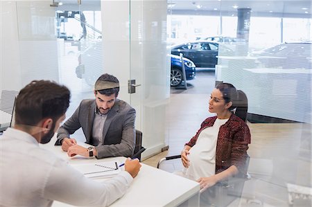 Car salesman explaining financial contract paperwork to pregnant couple customers in car dealership office Stock Photo - Premium Royalty-Free, Code: 6113-09111815