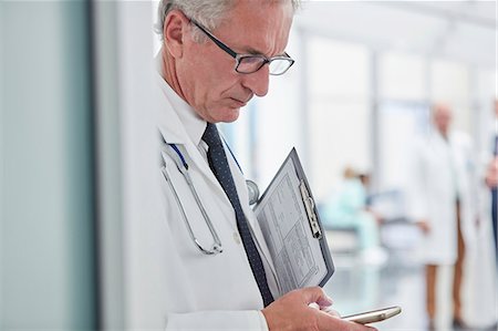 simsearch:6113-06720636,k - Male doctor with clipboard texting with smart phone in hospital Stock Photo - Premium Royalty-Free, Code: 6113-09111932