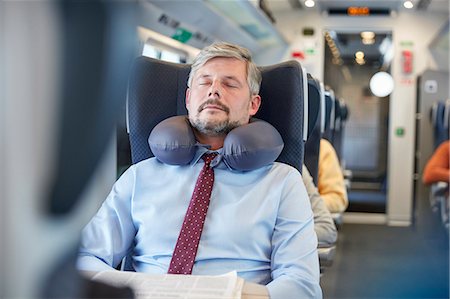 Tired businessman with neck pillow sleeping on passenger train Stock Photo - Premium Royalty-Free, Code: 6113-09131669