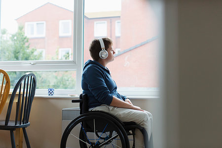 simsearch:6113-06909277,k - Thoughtful young woman in wheelchair listening to music with headphones at window Stock Photo - Premium Royalty-Free, Code: 6113-09240735