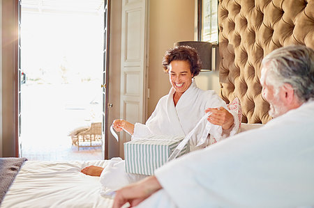 simsearch:6113-07242393,k - Husband watching happy wife opening gift on hotel bed Stock Photo - Premium Royalty-Free, Code: 6113-09241171