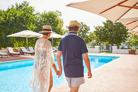 simsearch:6113-07242393,k - Mature couple holding hands, walking along sunny resort swimming pool Stock Photo - Premium Royalty-Free, Code: 6113-09241216