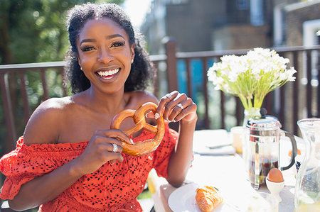 soft pretzel food photography - Portrait smiling, confident young woman with pretzel enjoying breakfast on sunny balcony Stock Photo - Premium Royalty-Free, Code: 6113-09220689