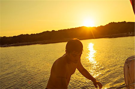 simsearch:6115-07539685,k - Croatia, Adriatic Sea, Young man on sailboat at sunset, leaving water Stock Photo - Premium Royalty-Free, Code: 6115-06733152